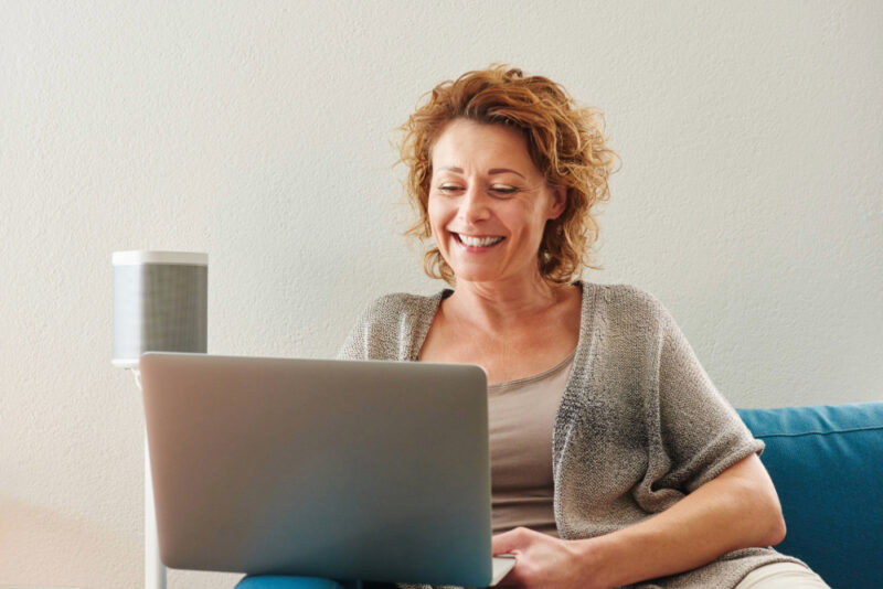 Frau sitzt lächelnt vor Laptop auf Sofa